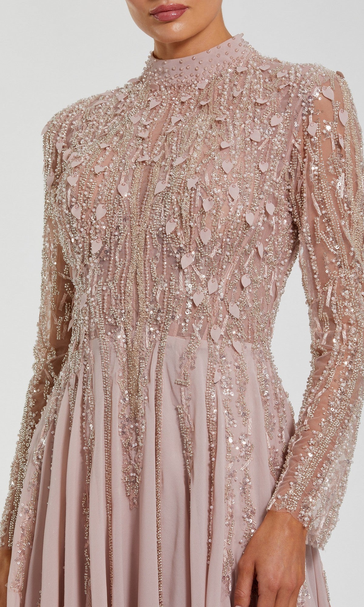 A woman wears the Mac Duggal 37037 long formal dress, a blush pink gown with intricate sequin and bead embellishments on the bodice and sleeves.